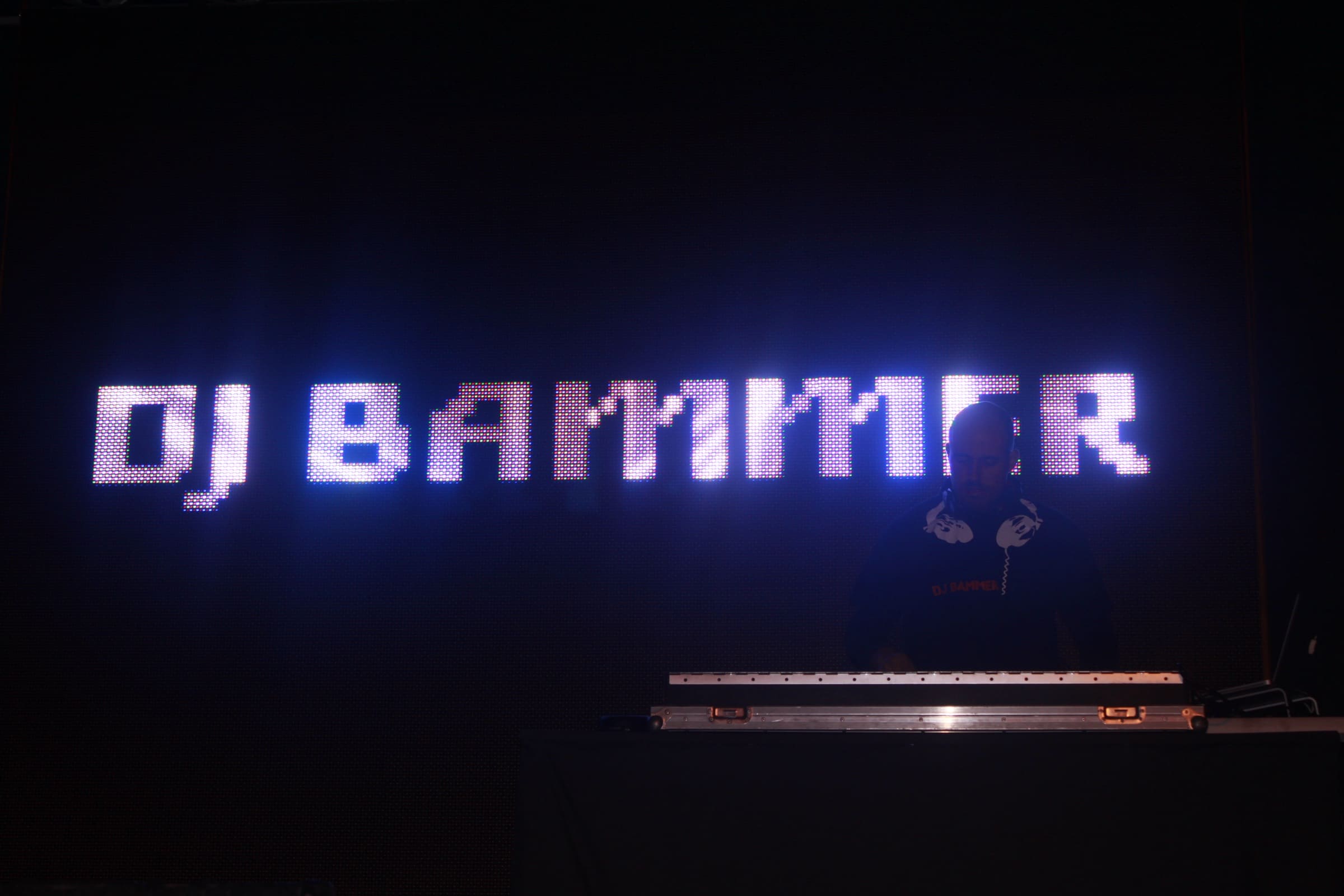 DJ Bammer at the decks under an LED wall spelling DJ BAMMER